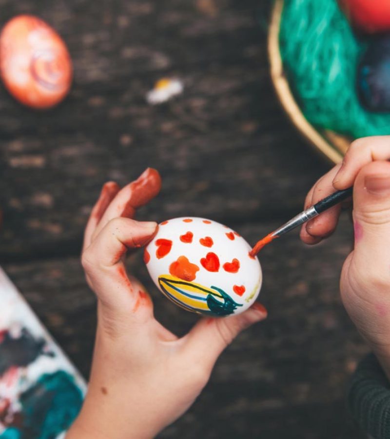 little girl painting easter egg on old wooden table Overhead view on Childs hand painting easter eggs on old wooden table
