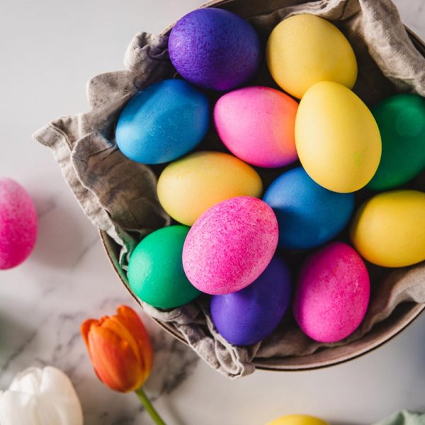 Colorful Easter eggs in basket with flowers on table Top view of colorful Easter eggs in basket and flowers on white marble table.