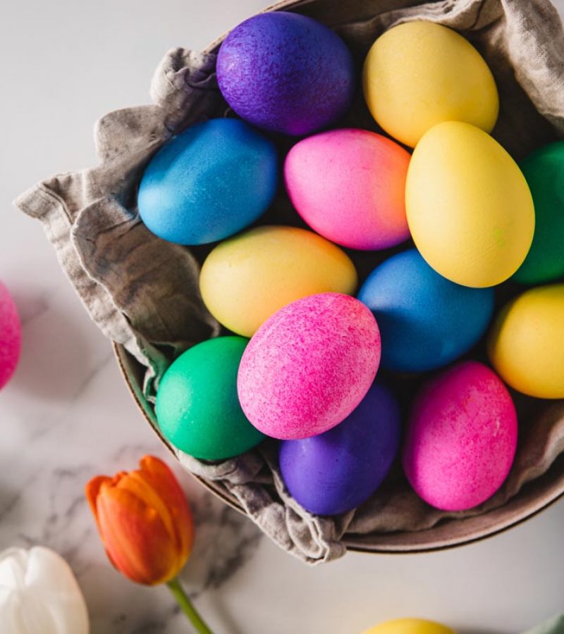 Colorful Easter eggs in basket with flowers on table Top view of colorful Easter eggs in basket and flowers on white marble table.